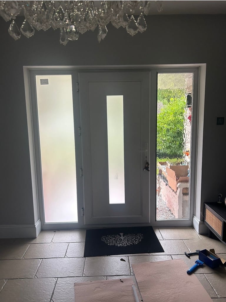 Modern gray patio doors with frosted panels opening to a garden, with a black doormat and decorative chandelier visible above