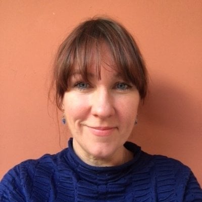 Portrait of Rosanna Hunt, smiling with brown hair and bangs wearing a dark blue sweater