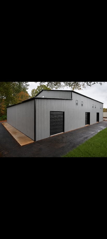 Modern gray metal warehouse building with black garage doors and windows on a paved driveway surrounded by grass and trees