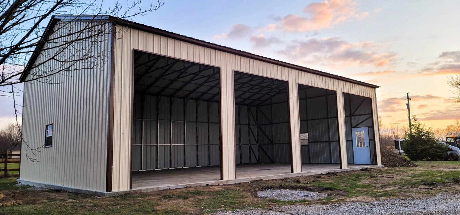 Metal industrial shed or equipment storage building with large open bay doors and white corrugated siding at dusk