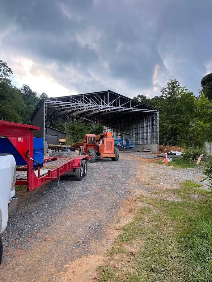 Construction site with red machinery and metal storage structure under cloudy sky surrounded by trees