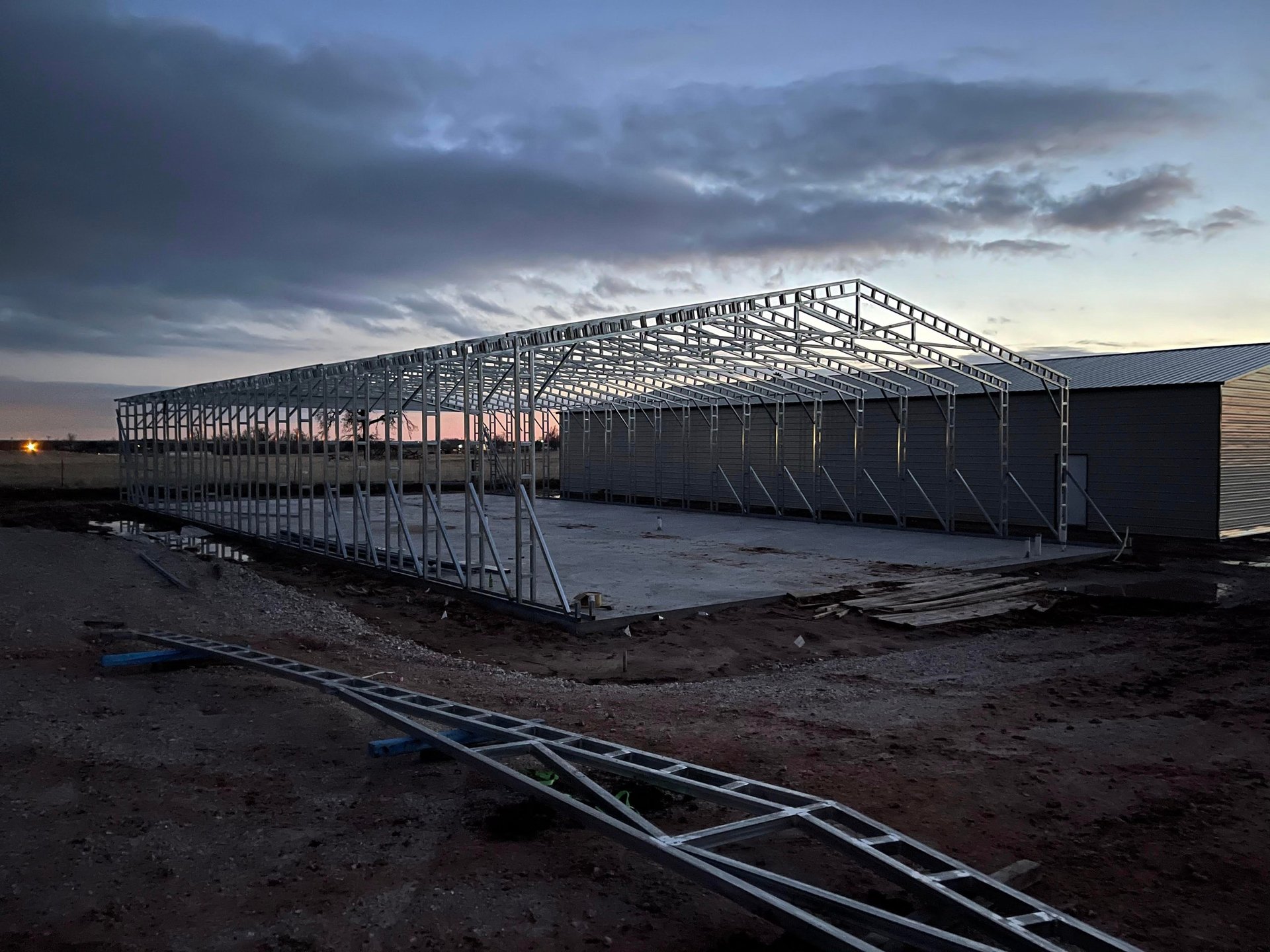 Industrial steel frame structure under construction at dusk with metal scaffolding, cables, and cloudy sky