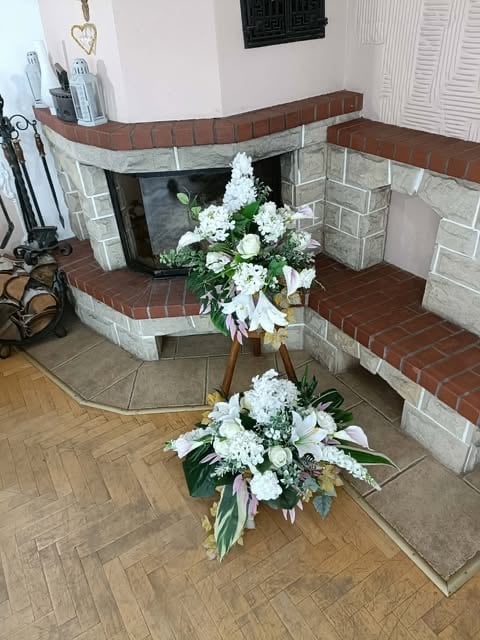 Dwie piętrowe białe kompozycje kwiatowe przed ceglanym kominkiem z białymi dekoracjami na półce