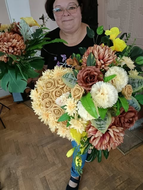 Kobieta trzymająca duży bukiet mieszanych kwiatów z kremowymi różami, koralowymi daliami i białymi stokrotkami w niebieskim wazonie