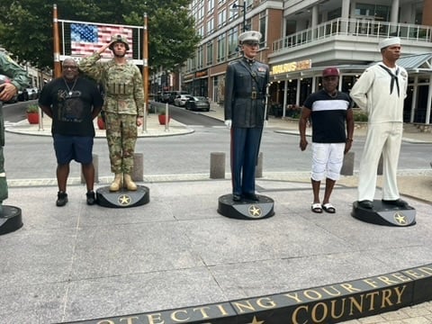 Life-size cardboard cutouts of military service members and personnel displayed on an urban plaza, honoring American armed forces