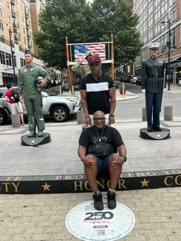 Man posing at Hollywood Walk of Fame star with military uniform statues in background on city street