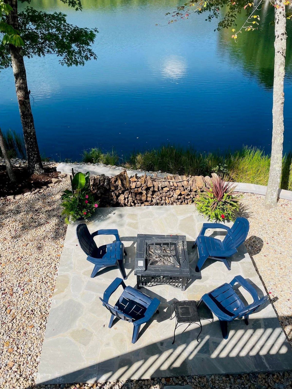 Four blue chairs arranged around a fire pit on a stone patio overlooking a calm lake — the kind of outdoor living space financing makes possible