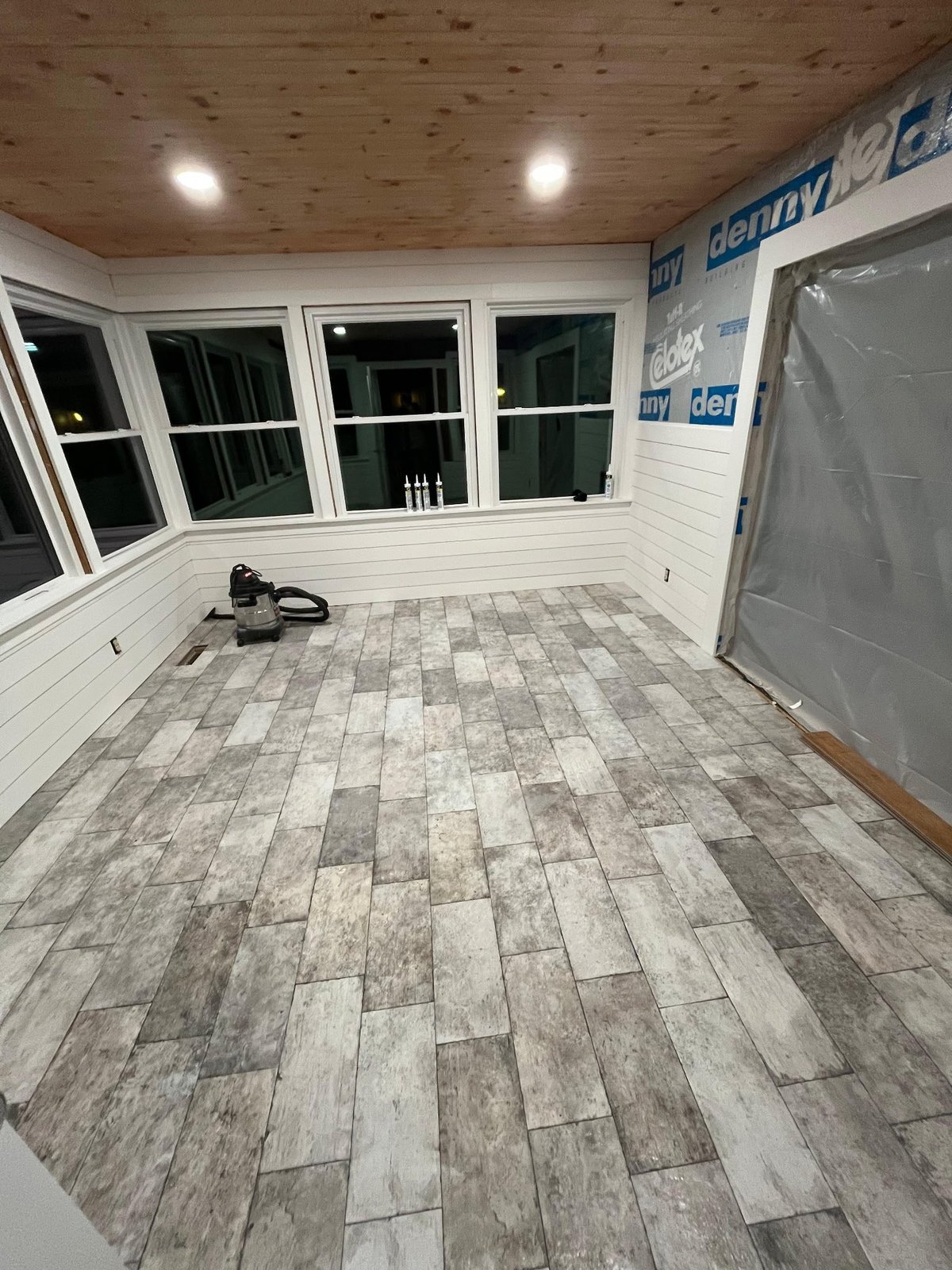 Empty sunroom under construction with wood plank tile flooring, white walls, and large windows