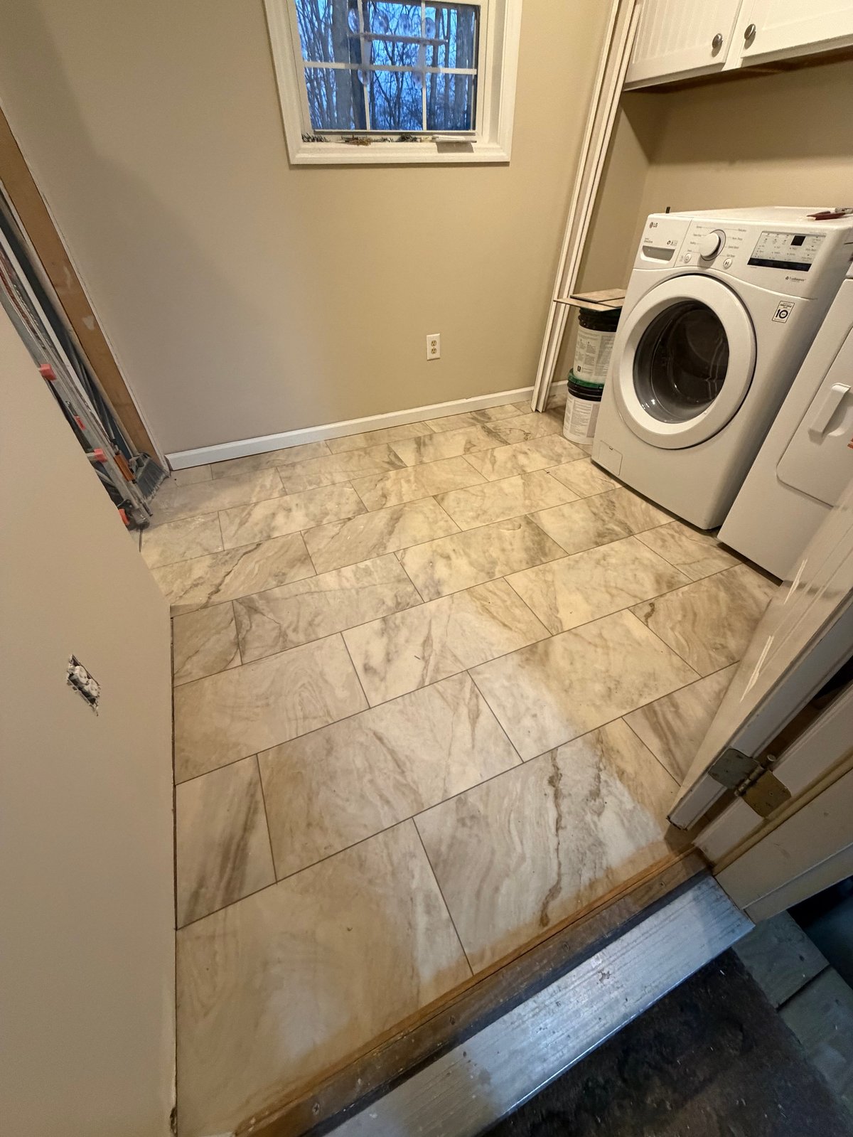 Modern laundry room with beige walls, marble tile flooring, white front-load washer and dryer