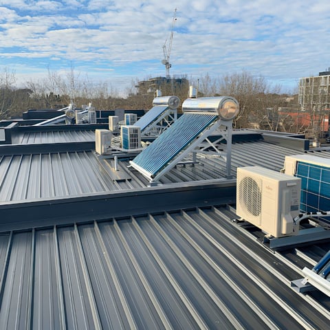 Industrial rooftop with solar panels, HVAC unit, and communication tower against cloudy sky