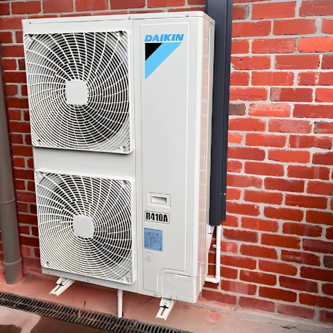 Daikin outdoor AC unit mounted on red brick wall with dual fan compressors and white casing