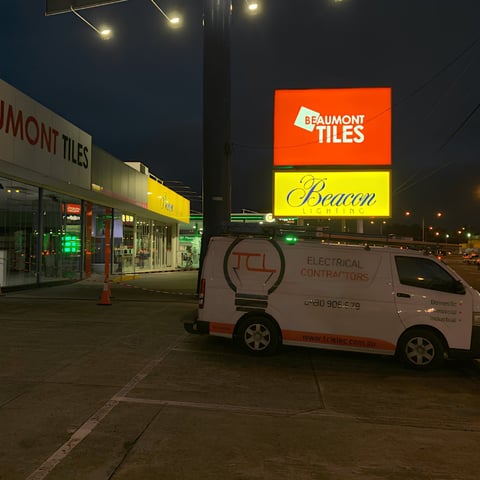 White TCL electrical van parked at night in front of illuminated Beaumont Tiles storefront sign