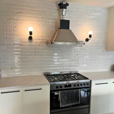 Modern kitchen with white subway tile backsplash, black gas range, stainless steel range hood, and sconce lighting on either side