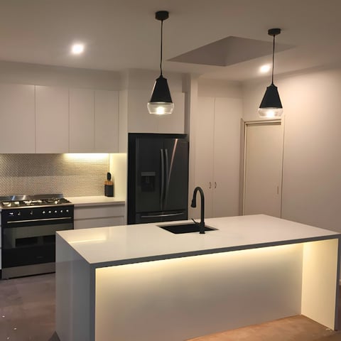 Modern kitchen with white island countertop, black range and refrigerator, pendant lights, and recessed ceiling lights