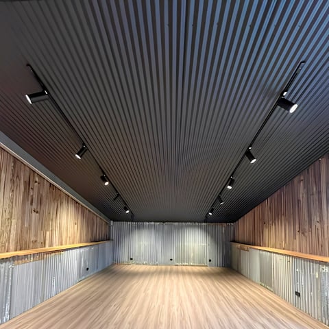 Interior of a storage unit or garage with corrugated metal walls, wooden flooring, dark ceiling, and recessed lighting