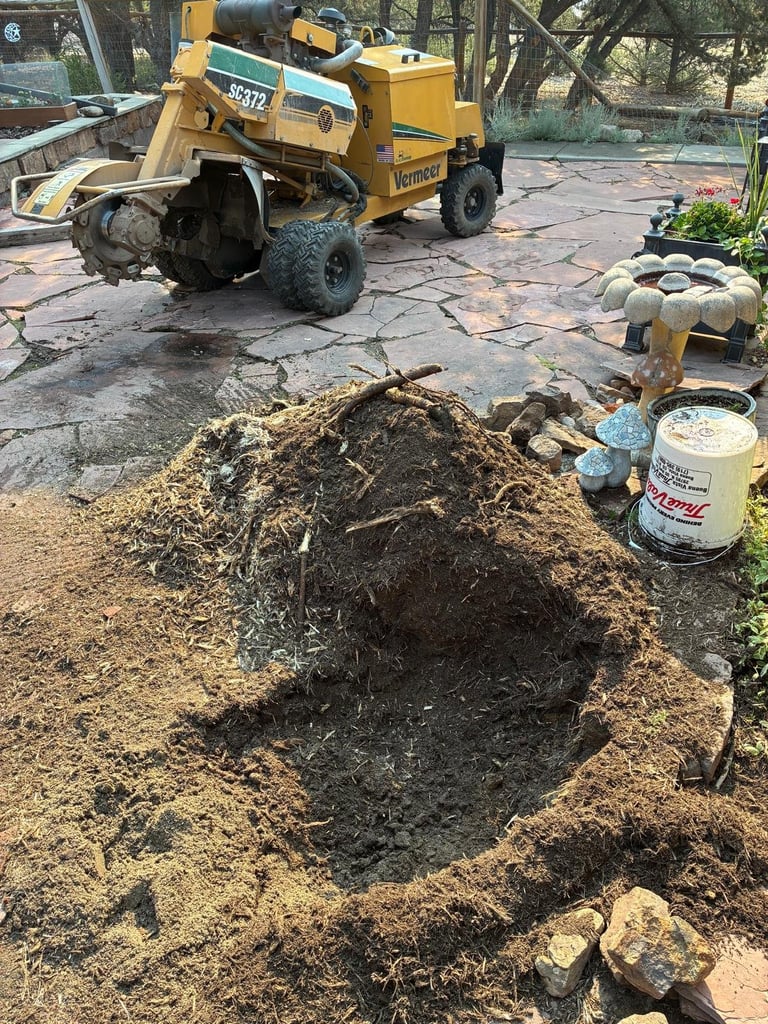 Yellow wood chipper machine processing branches into a mulch pile on a work site with landscaping equipment