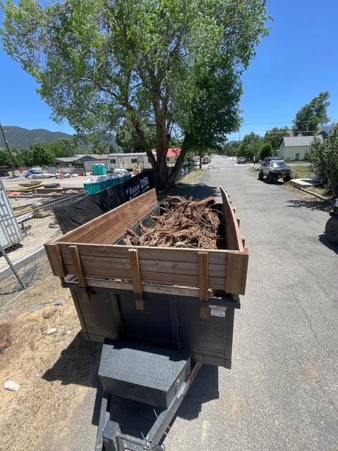 Wooden trailer filled with wood chips and debris parked in a rural yard on a sunny day