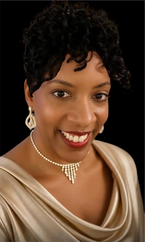 Portrait of a woman with short curly black hair, pearl jewelry, and red lipstick smiling against a black background
