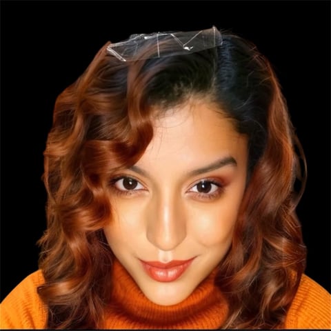 Portrait of a woman with reddish-brown wavy hair, glasses on her head, wearing an orange turtleneck against a black background