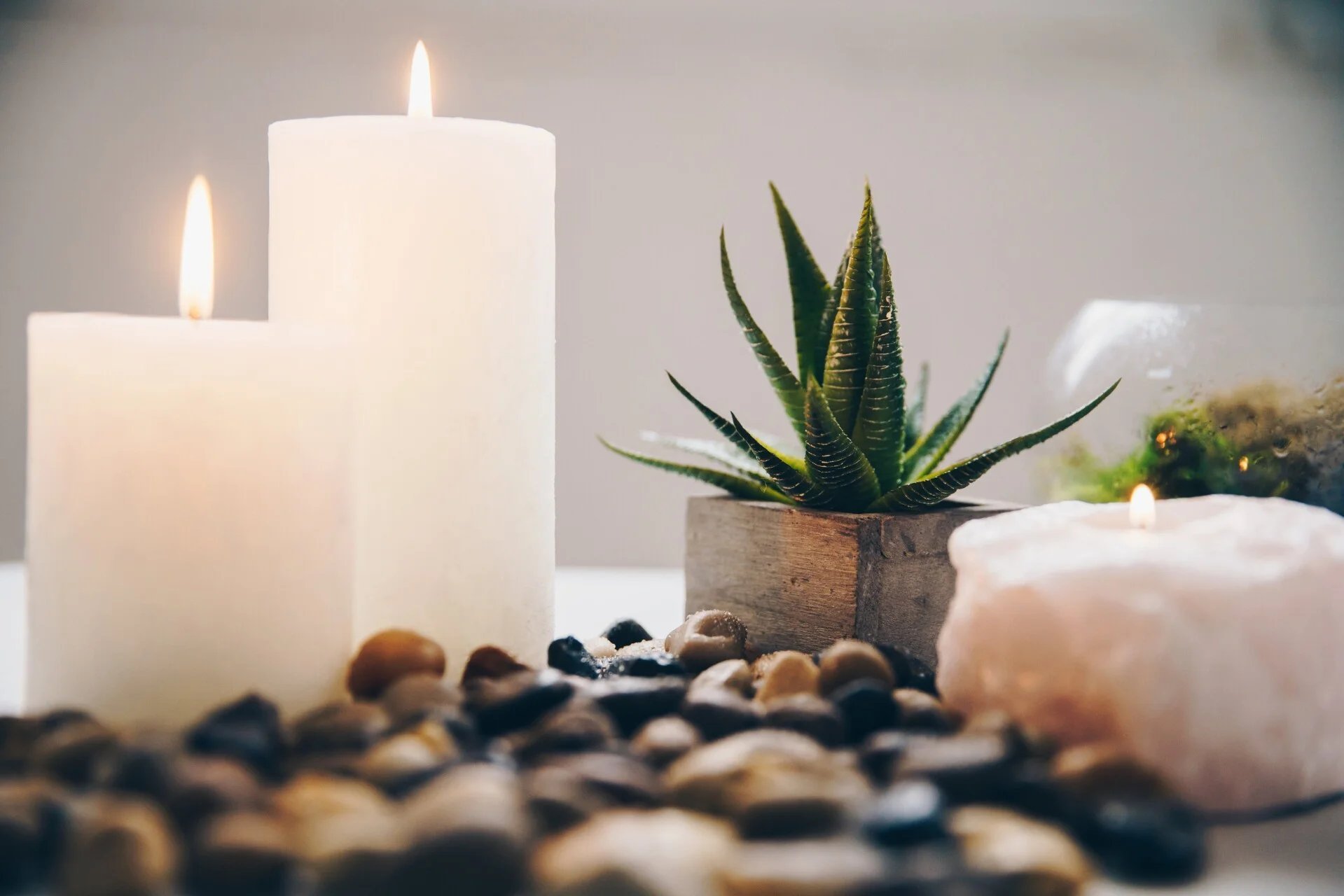 Spa and wellness arrangement with lit candles, potted succulent plant, decorative stones, and a white shell on a neutral surface