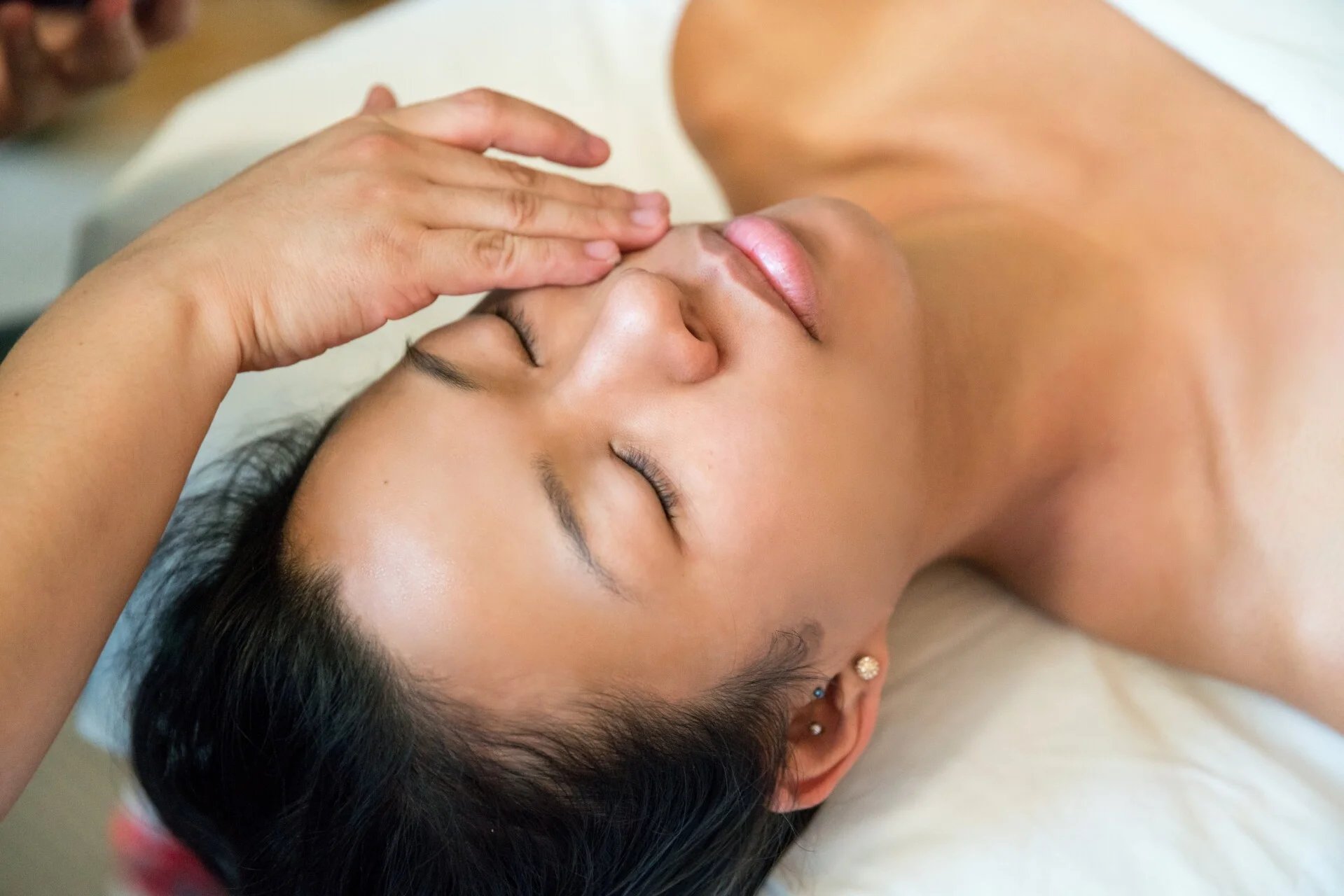 Person lying down receiving a facial massage or beauty treatment on the face with eyes closed