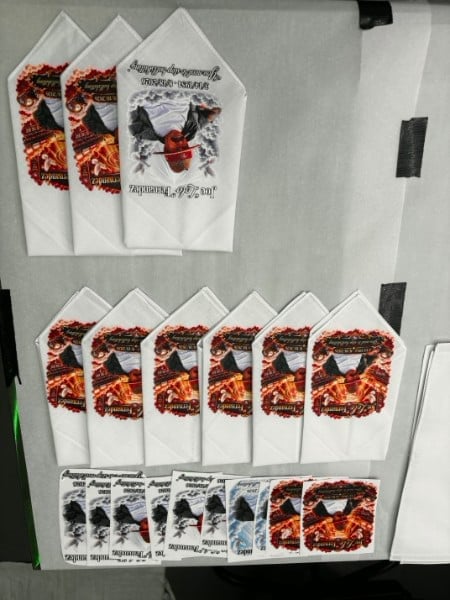 Collection of white cloth items with red graphic designs and text displayed on a gray surface for product presentation