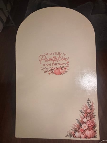 Cream-colored greeting card with arched top featuring text A Little Peachfuzz Is On The Way and floral pumpkin illustrations in pink and green