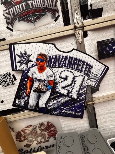 Baseball jersey-shaped sticker of player Navarrete #27 on wooden desk with other stickers and decor