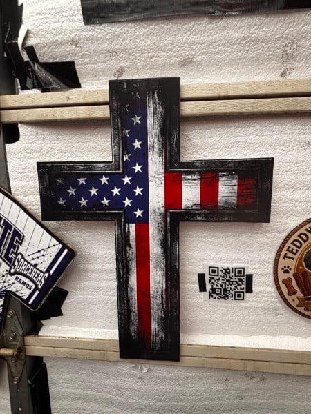 Wooden cross with American flag design displayed on white textured wall with tan horizontal beams