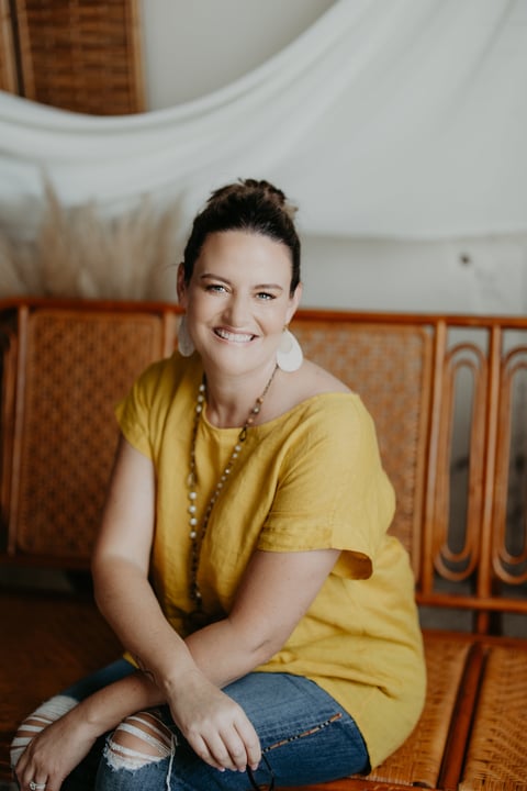 Woman in yellow shirt sitting on mid-century modern furniture, smiling at camera with white pillows and wood paneling in background