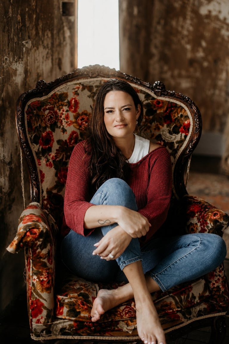Woman in red sweater and jeans sitting on ornate vintage floral chair in industrial setting
