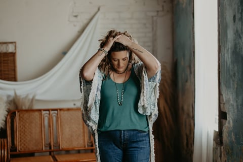 Woman in teal top and jeans adjusting lace cardigan in rustic industrial interior