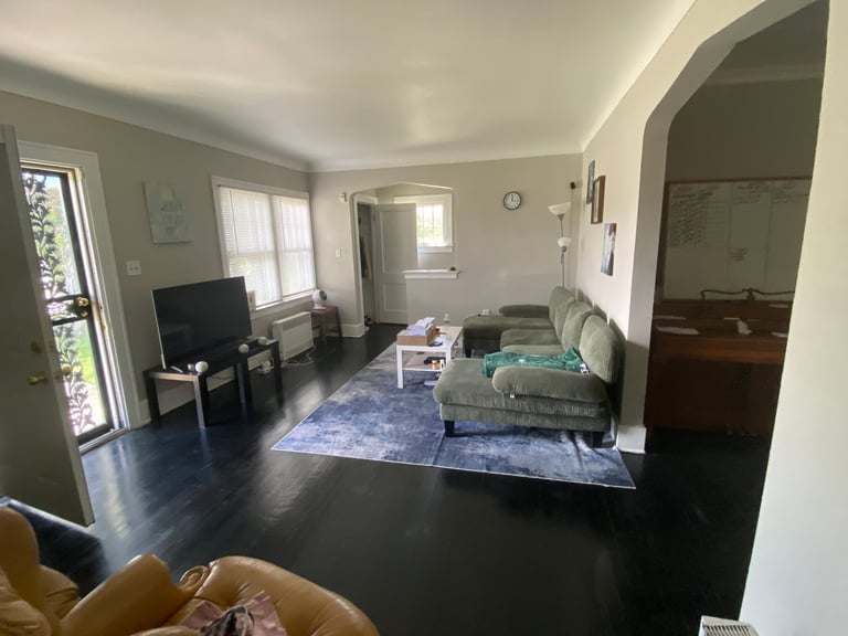 Spacious living room with dark hardwood floors, green upholstered furniture, TV, windows with natural light, and an arched doorway