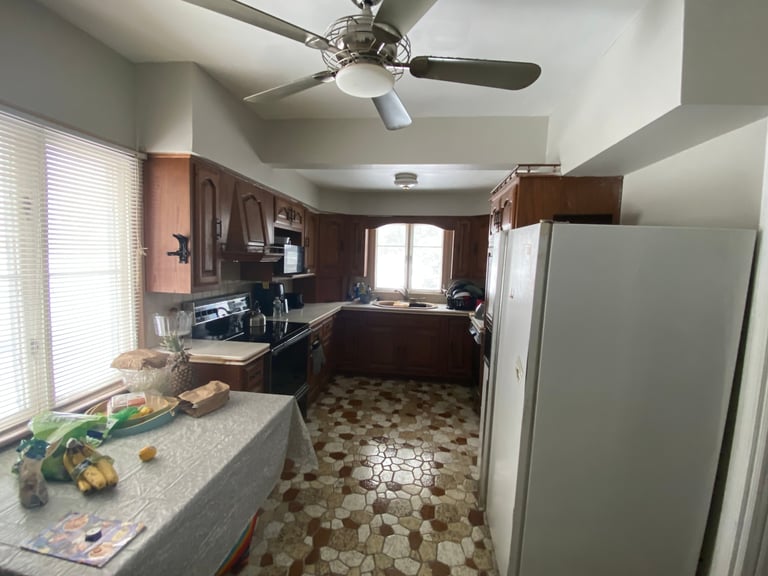 Modern kitchen interior with wood cabinets, stainless steel refrigerator, granite countertops, and ceiling fan