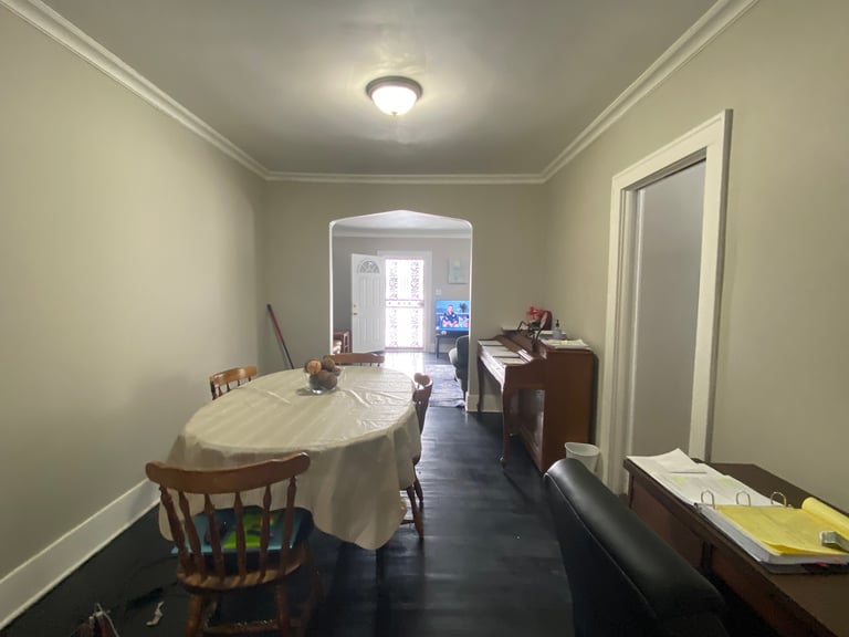 Long narrow room with pale green walls, wood furniture, round table with white cloth, wooden chairs, and doorways at far end