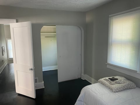 Modern bedroom with gray walls, white bed, mirrored wardrobe, white door, and window with blinds
