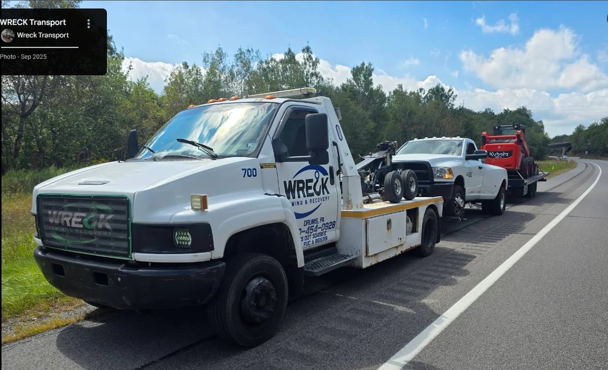 White GMC wreck truck towing vehicles on a highway with trees and clear sky in the background