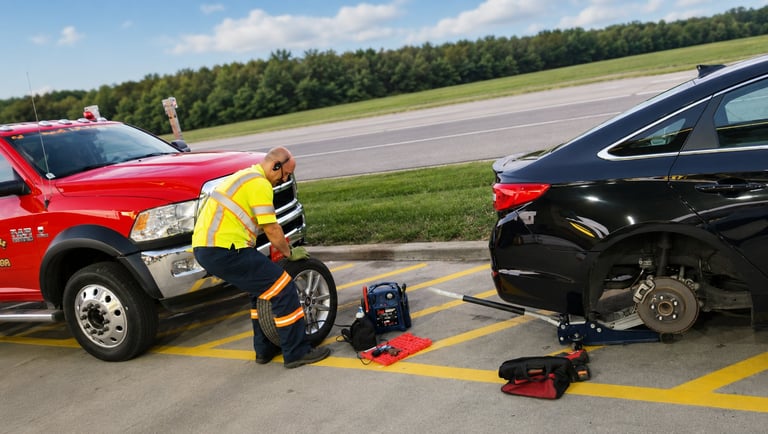 Emergency responder in yellow gear documenting vehicle accident scene between red and black cars on road