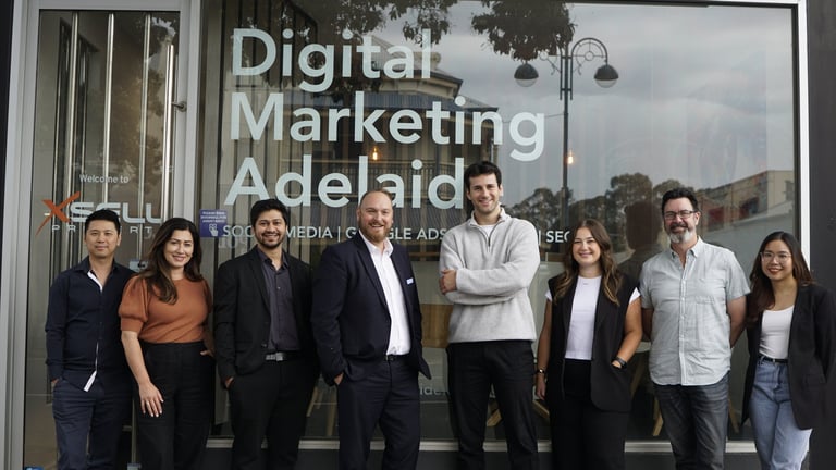 Team of eight professionals posing in front of Digital Marketing Adelaide storefront window