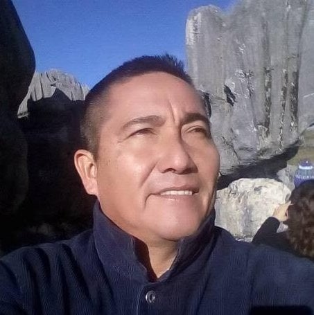 Man smiling at camera outdoors with concrete wall in background under blue sky
