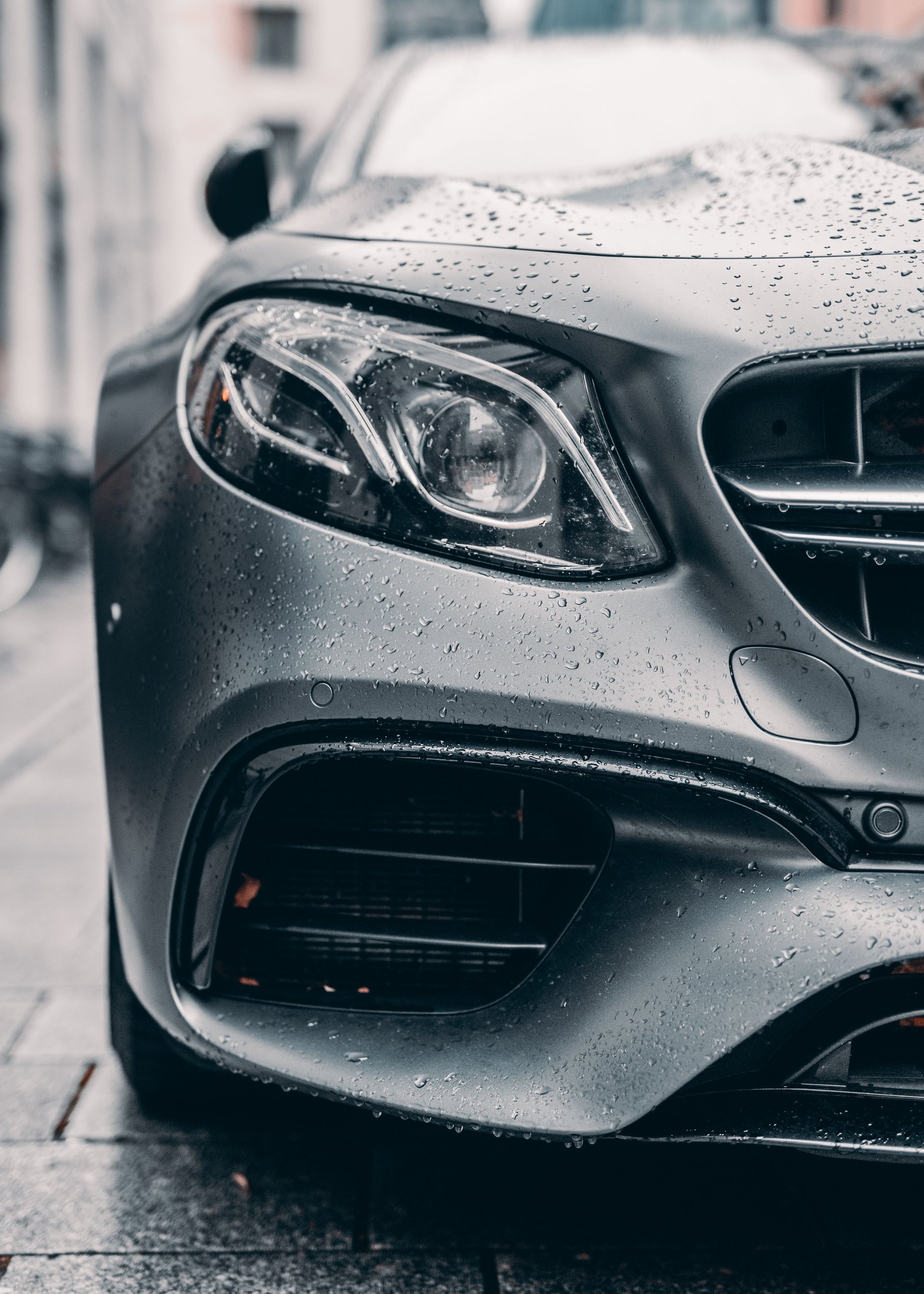 Close-up of a silver Mercedes-AMG sports car wet with raindrops, showing the front headlight and grille details
