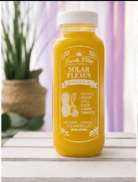 Bottle of Fresh Vibe Sun Plexus golden juice drink on windowsill with potted plant in background