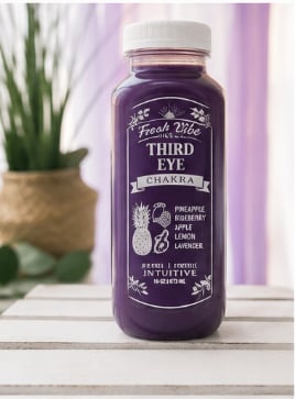 Bottle of Third Eye purple juice blend with pineapple and other fruit ingredients on white surface with green plant