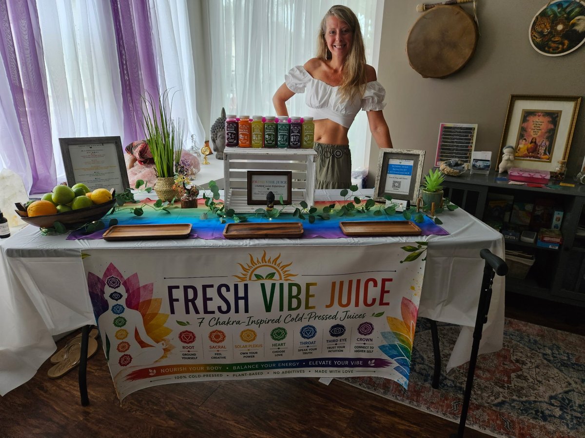 Woman standing behind Fresh Vibe Juice juice bar display with colorful bottles, fresh produce, and promotional banner