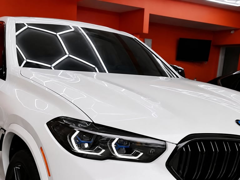 White luxury SUV with LED headlights and geometric window tint displayed in showroom with red walls