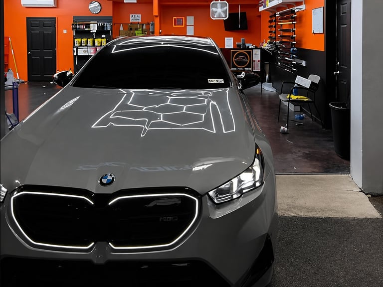Gray BMW sedan parked in an orange-walled automotive workshop with tools and equipment visible in the background