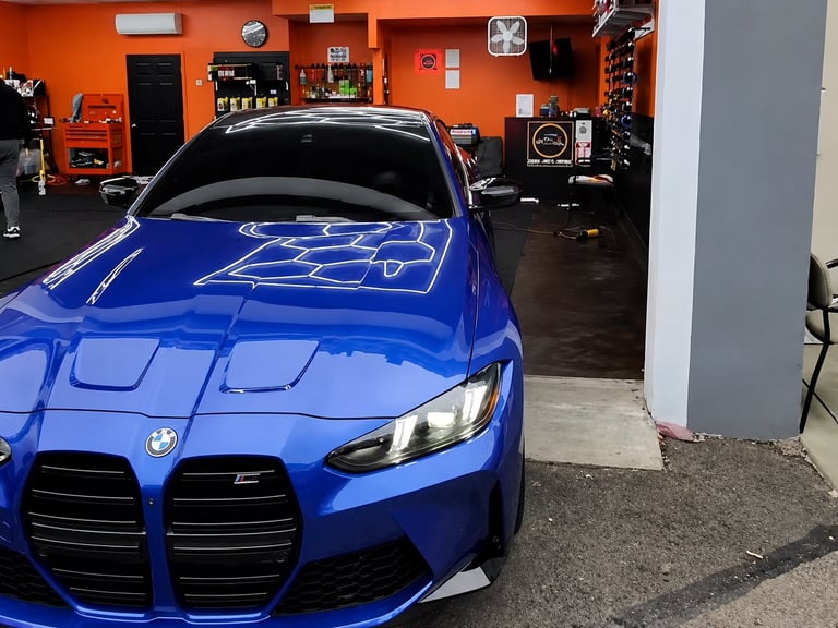 Blue BMW sports car parked in an orange-walled automotive garage with racing memorabilia and equipment