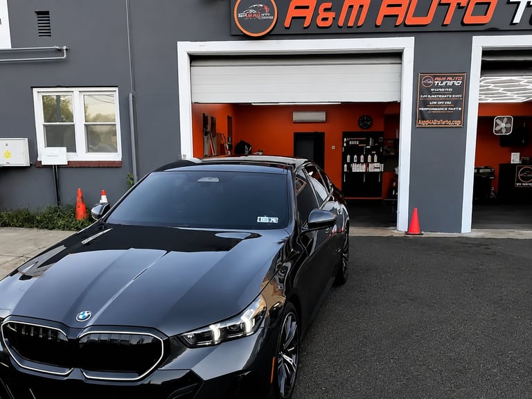 Black BMW sedan parked outside an auto shop with orange garage interior and gray storefront