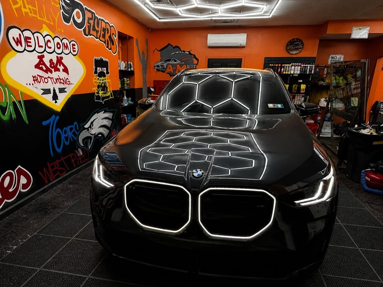 Black BMW sports car with glowing neon outline displayed in a colorful garage showroom with orange walls and neon signs