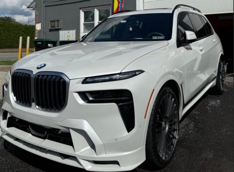 White BMW X7 luxury SUV parked outside a dealership with distinctive kidney grille and dark alloy wheels